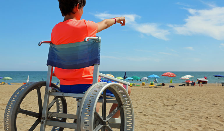 child in wheelchair on beach, pointing at water