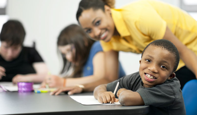 child in classroom at desk with teacher