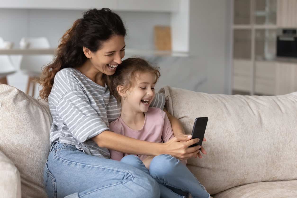 mother with daughter on sofa smiling, looking at smartphone